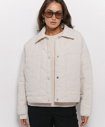 Cropped women's light beige transitional quilted jacket with wavy stitching.