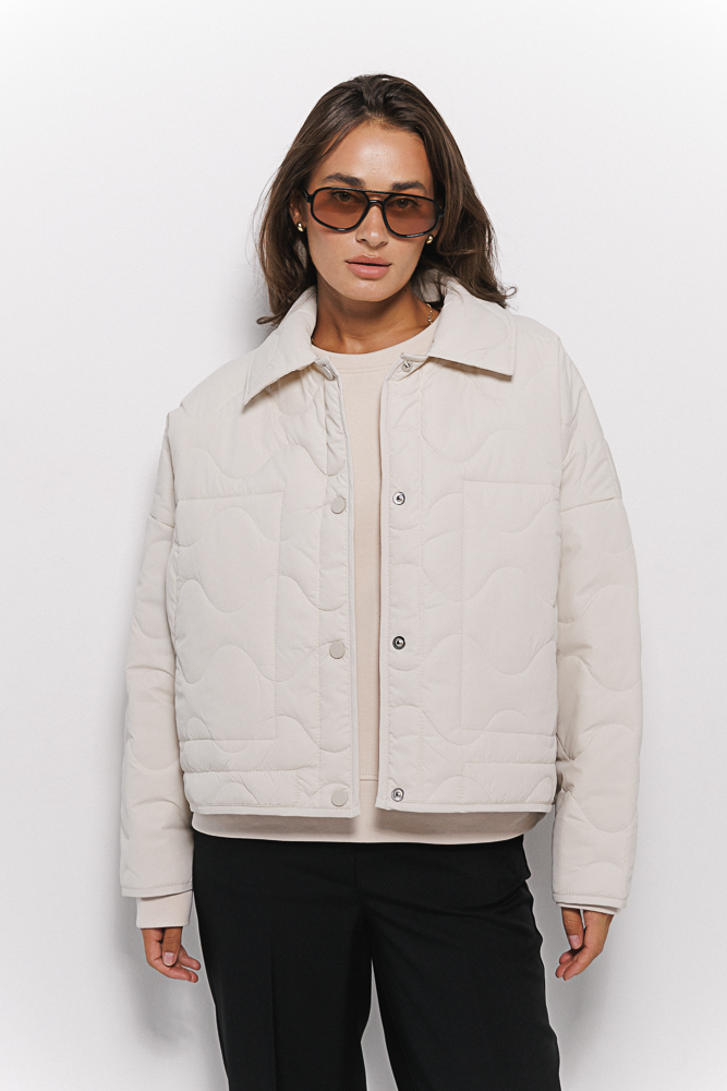 Cropped women's light beige transitional quilted jacket with wavy stitching.