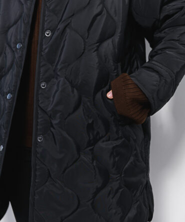 Women's elongated black quilted jacket with a wave pattern.