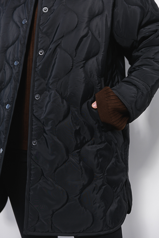 Women's elongated black quilted jacket with a wave pattern.